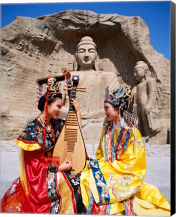 Framed Two girls in traditional costumes in front of the Buddha Statue, China Print