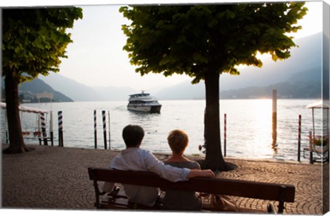 Framed Couple sitting on bench and watching ferry approaching dock along the Lake Como, Bellagio, Province of Como, Lombardy, Italy Print