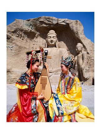 Framed Two girls in traditional costumes in front of the Buddha Statue, China Print