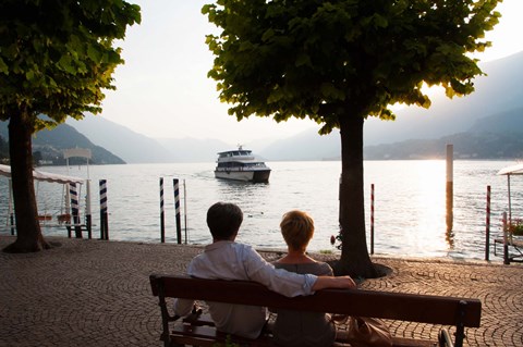 Framed Couple sitting on bench and watching ferry approaching dock along the Lake Como, Bellagio, Province of Como, Lombardy, Italy Print