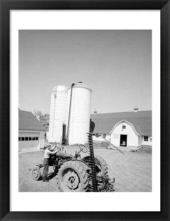 Framed USA, Farmer Working on Tractor, Agricultural Buildings in the Background Print