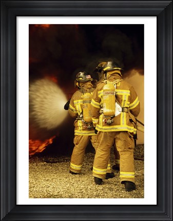 Framed Rear view of three firefighters extinguishing a fire Print
