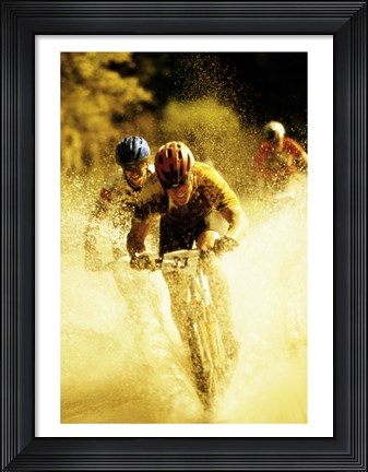 Framed Young men riding bicycles through water Print