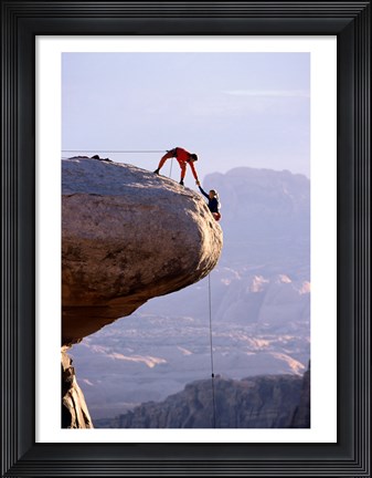 Framed Side profile of a young man pulling a young woman onto a rock Print