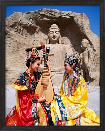 Framed Two girls in traditional costumes in front of the Buddha Statue, China Print