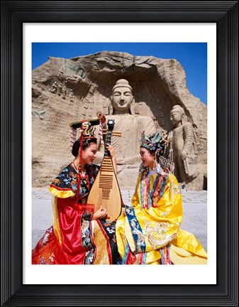 Framed Two girls in traditional costumes in front of the Buddha Statue, China Print