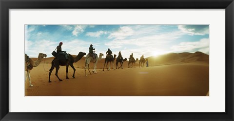 Framed Tourists riding camels through the Sahara Desert landscape led by a Berber man, Morocco Print