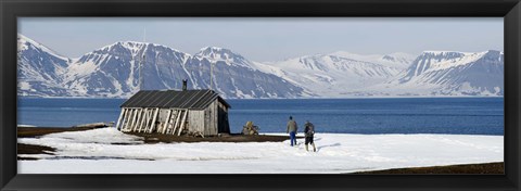 Framed Two hikers standing on the beach near a hunting cabin, Bellsund, Spitsbergen, Svalbard Islands, Norway Print