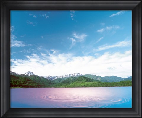 Framed Pink light cast down on two rings in lavender water with deep blue sky and clouds over green mountains in distance Print