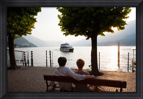 Framed Couple sitting on bench and watching ferry approaching dock along the Lake Como, Bellagio, Province of Como, Lombardy, Italy Print