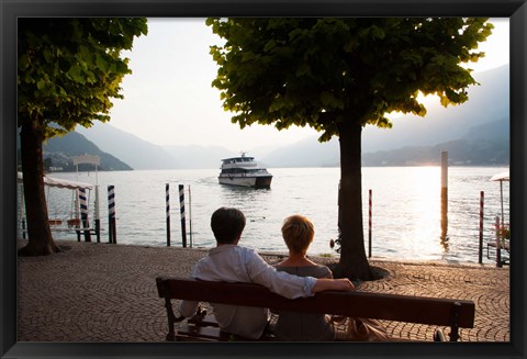 Framed Couple sitting on bench and watching ferry approaching dock along the Lake Como, Bellagio, Province of Como, Lombardy, Italy Print