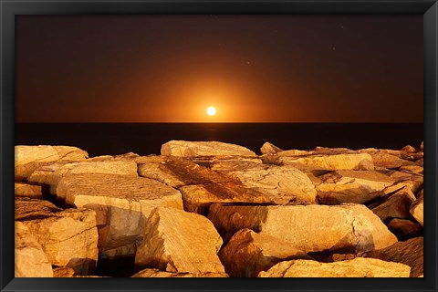 Framed moon rising behind rocks lit by a nearby fire in Miramar, Argentina Print