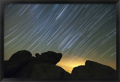 Framed Light pollution illuminates the sky and star tails above large boulders Print